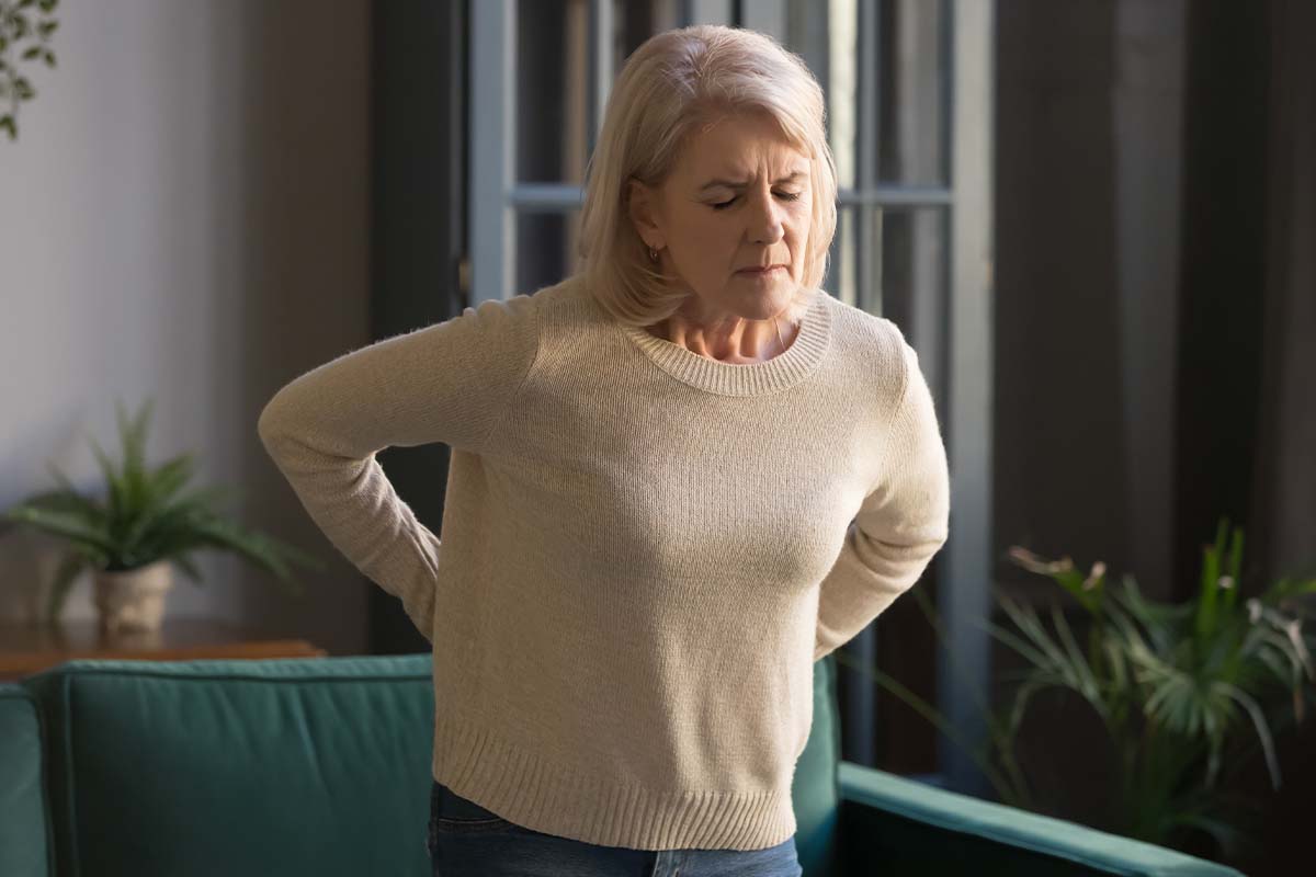 A woman stands up and rubs her lower back, her eyes are shut in pain due to fibromyalgia in Thousand Oaks