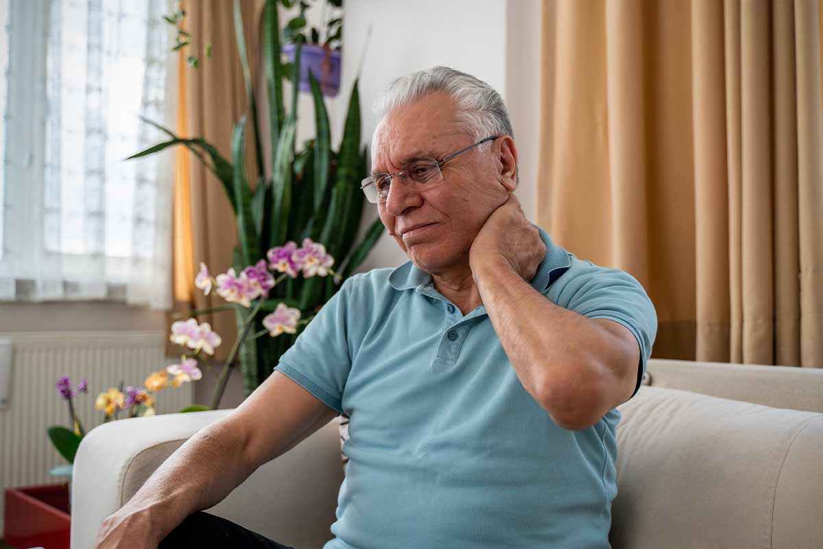 A man sits on a couch rubbing the back of his neck in pain, due to fibromyalgia in Thousand Oaks