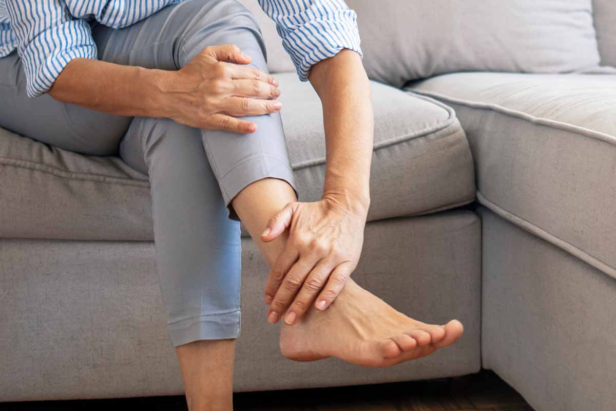A woman sitting on a couch grasping her ankle which requires rheumatoid arthritis treatment in Thousand Oaks